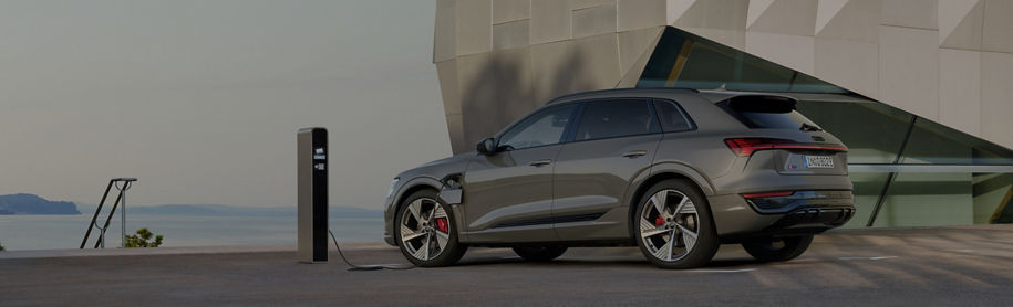 A parked Audi electric vehicle at a charge point in a coastal setting